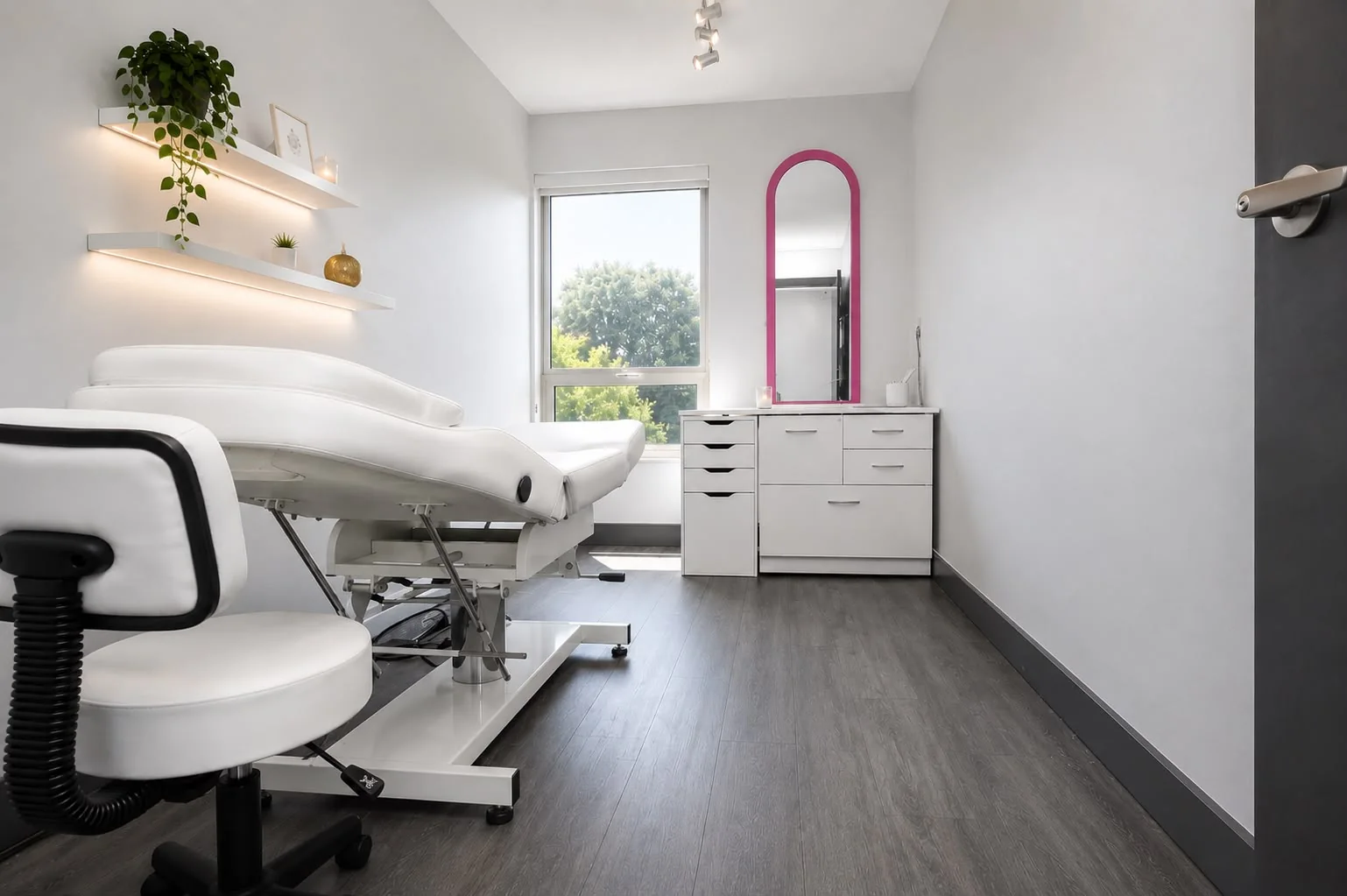 Private treatment room with white bed, fuchsia mirror and lit shelving
